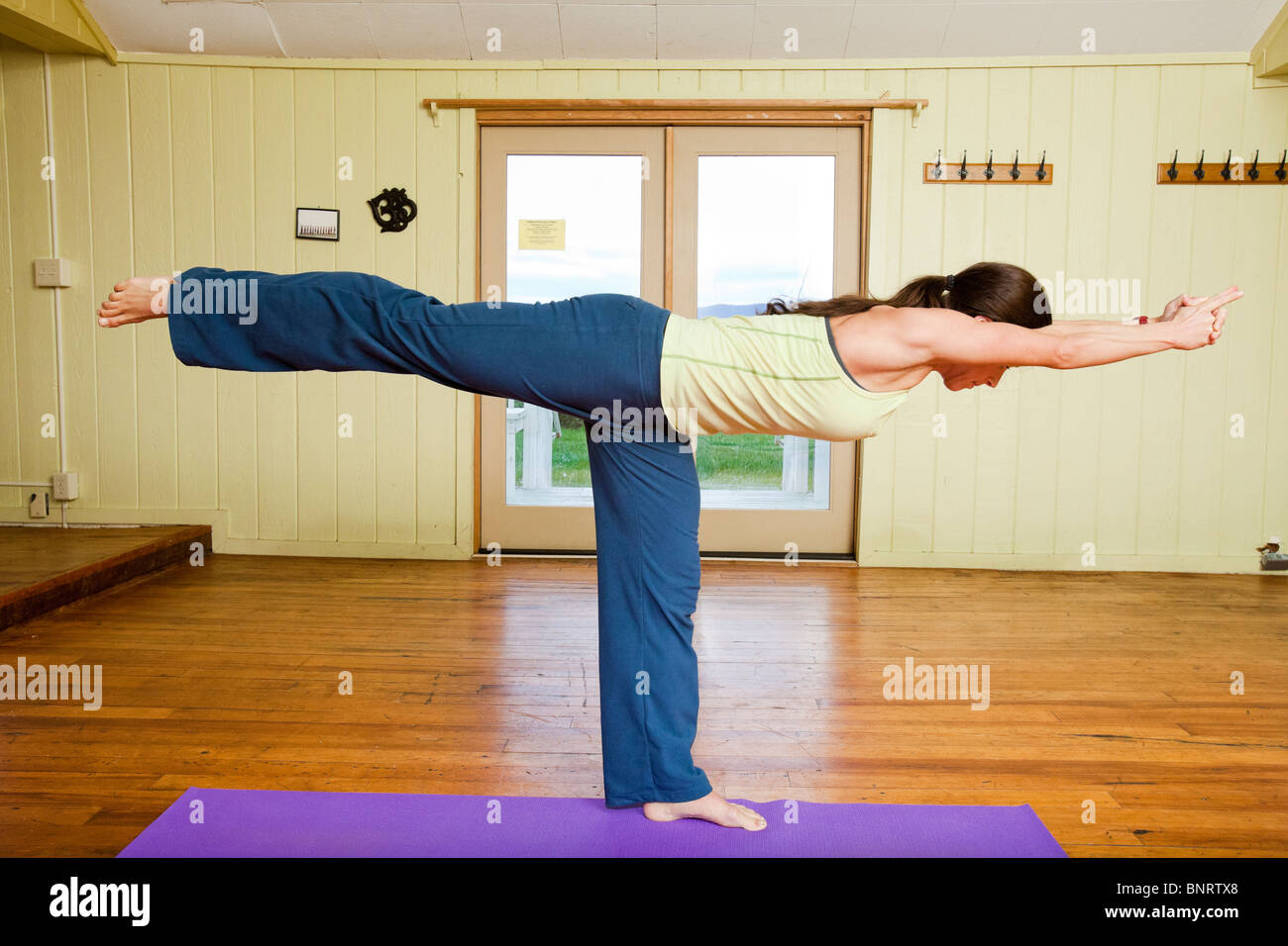 Una giovane donna si allunga se stessa in posizione orizzontale in un yoga posa in un piccolo studio. Foto Stock