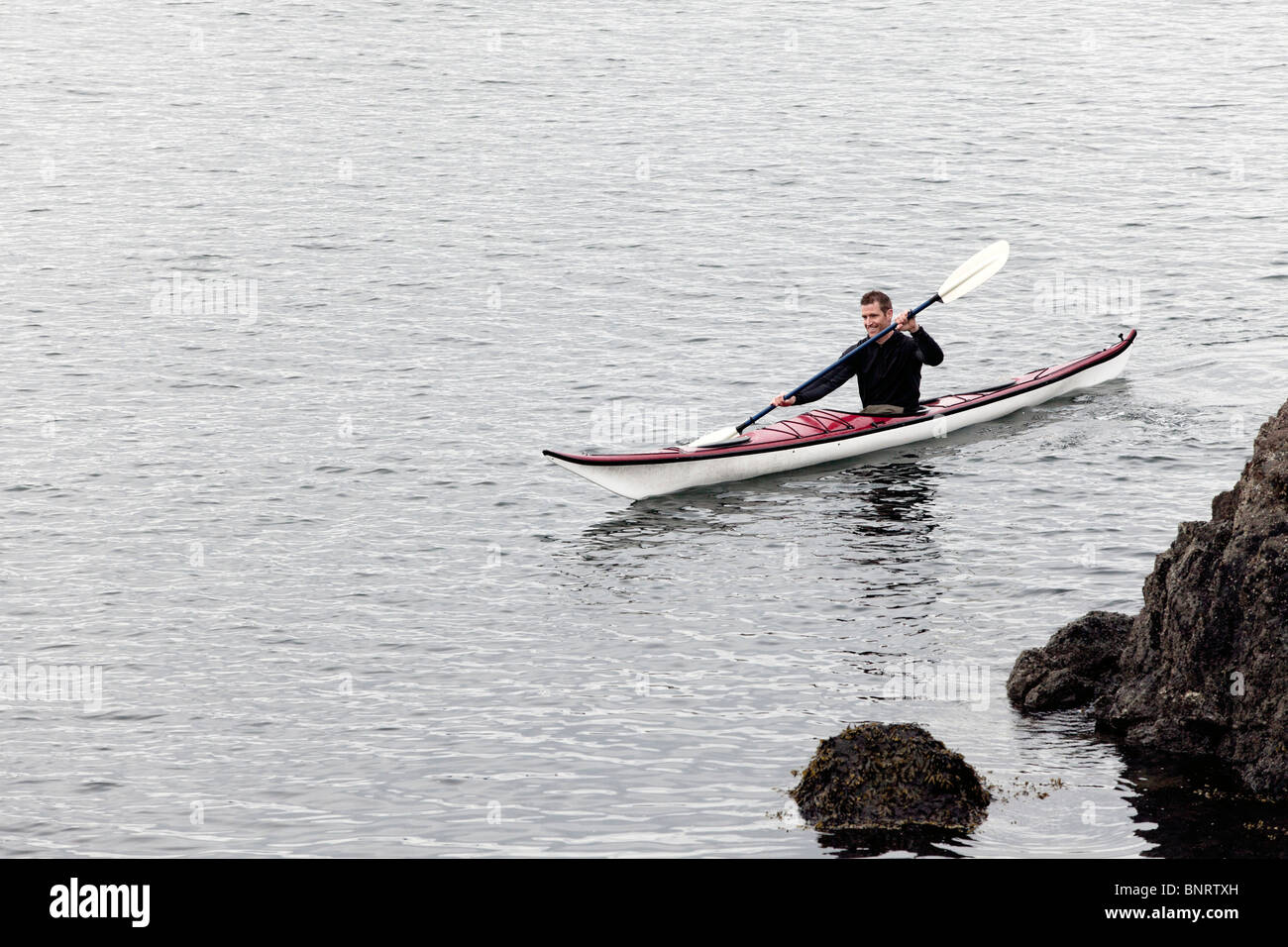 Un giovane uomo gode del Puget Sound intorno a San Juan Islands da kayak di mare. Foto Stock