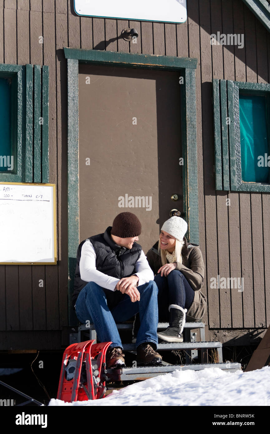 Un uomo e una donna si siedono sui gradini della porta con le racchette da neve e godersi la giornata. Foto Stock