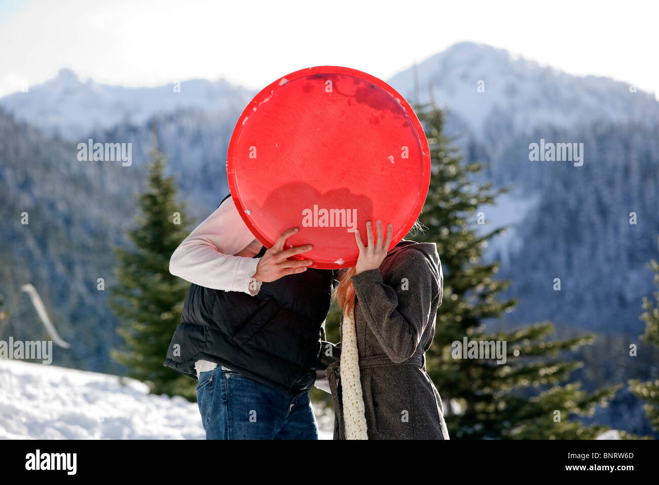 Un uomo e una donna si stagliano dietro di loro sled come essi kiss dopo slittino in montagna. Foto Stock