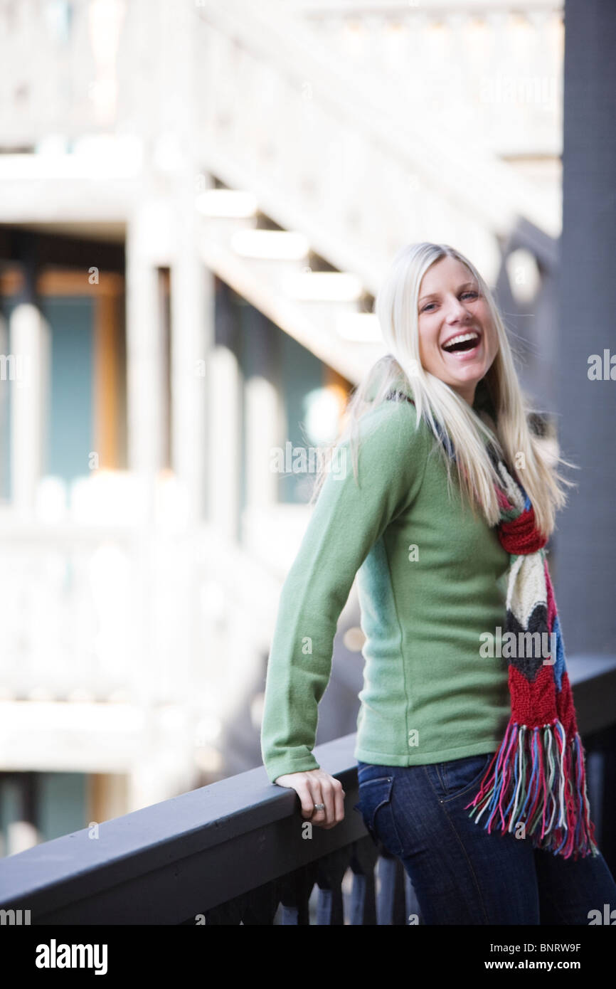 Una giovane donna con capelli biondi ride e sorrisi durante i momenti di relax nei pressi di una ringhiera di un Ski lodge. Foto Stock