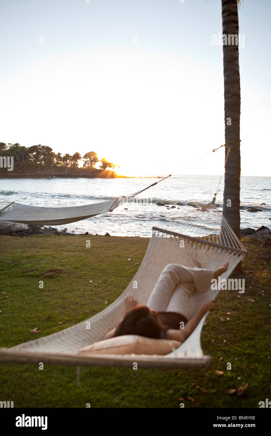 Un Latino adolescente si rilassa in un amaca in riva al mare al tramonto. Foto Stock