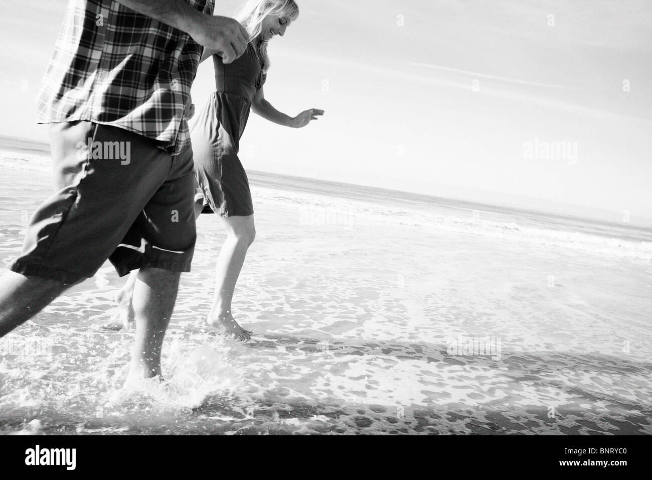 Giovane gestito dall'acqua e ottenere i loro piedi bagnati in spiaggia. Foto Stock