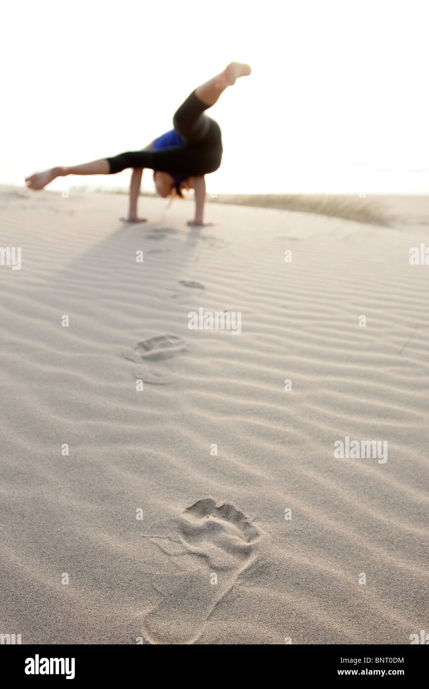 Una donna fare yoga, lascia orme mentre si cammina attraverso la sabbia. Foto Stock