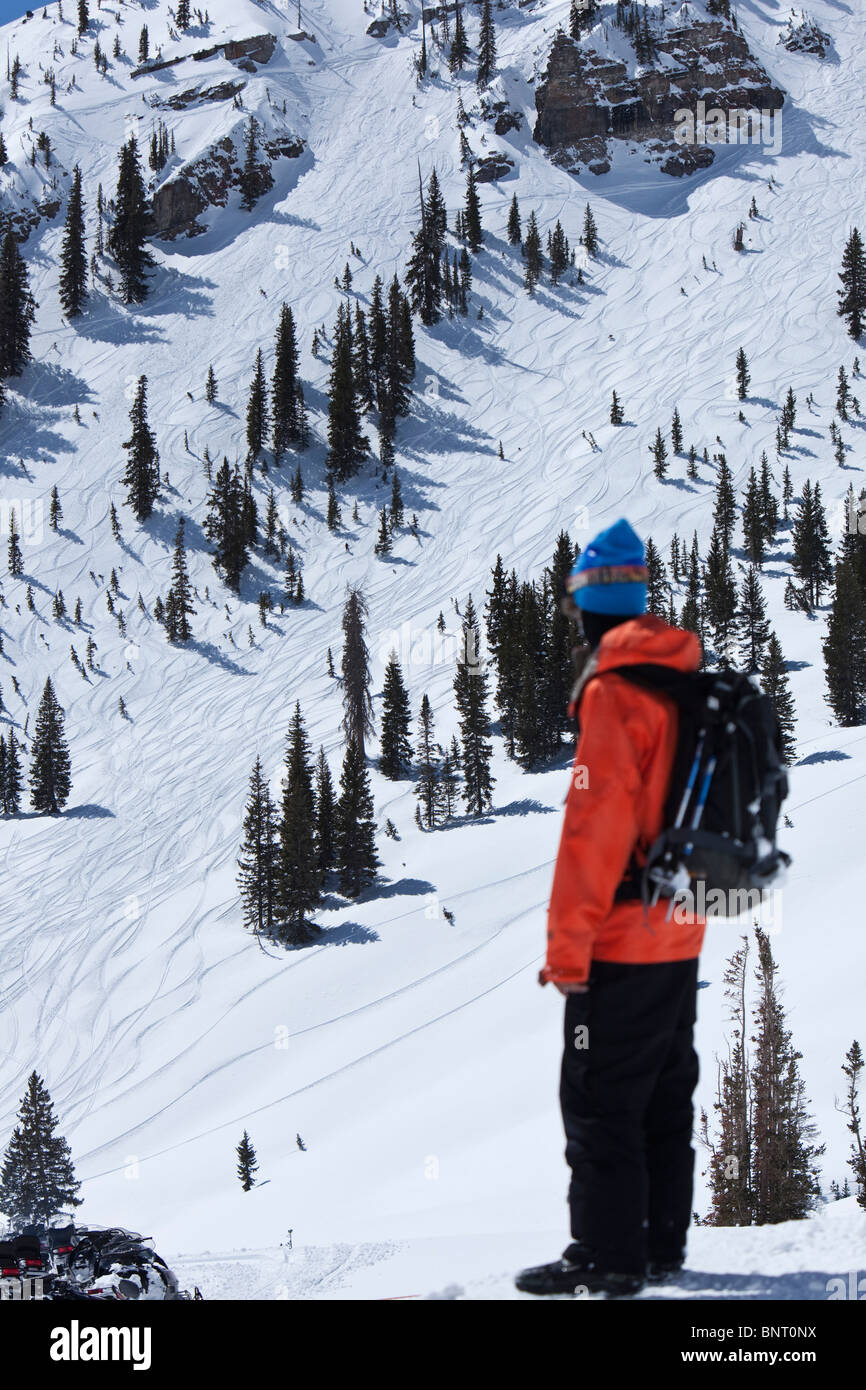 Un maschio di snowboarder si guarda indietro a una massiccia rupe solo andato fuori in Utah. Foto Stock