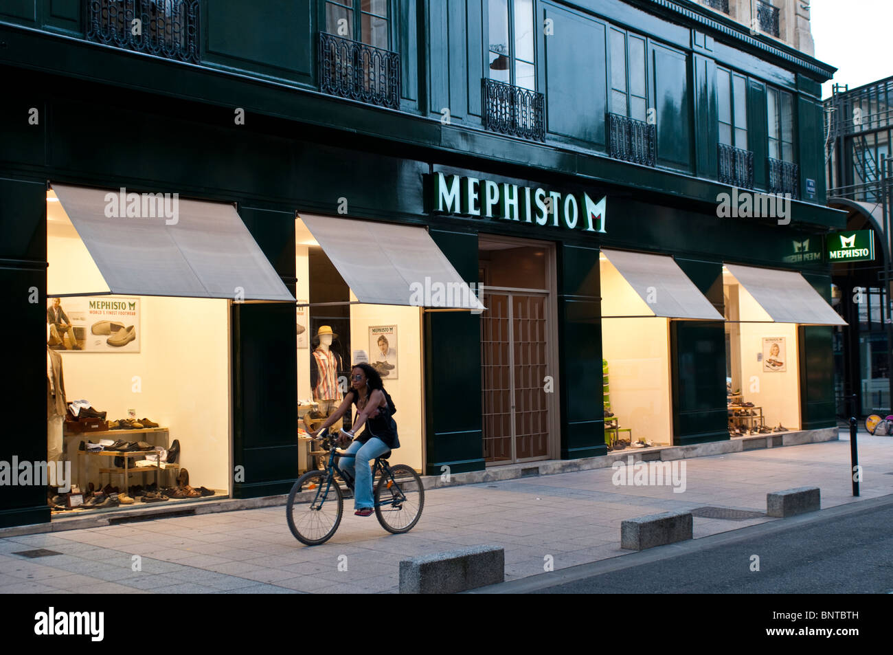 La donna in sella ad una bicicletta di fronte Mephisto M shop, Bordeaux, Francia Foto Stock