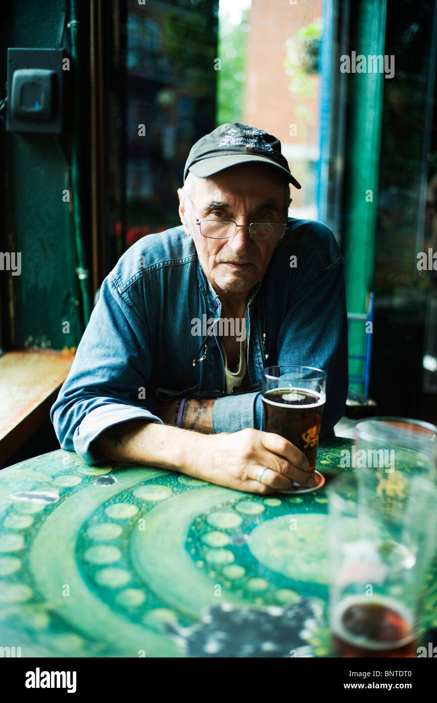 Il vecchio uomo a tavola nel bar con la mano su una pinta di birra. Foto Stock