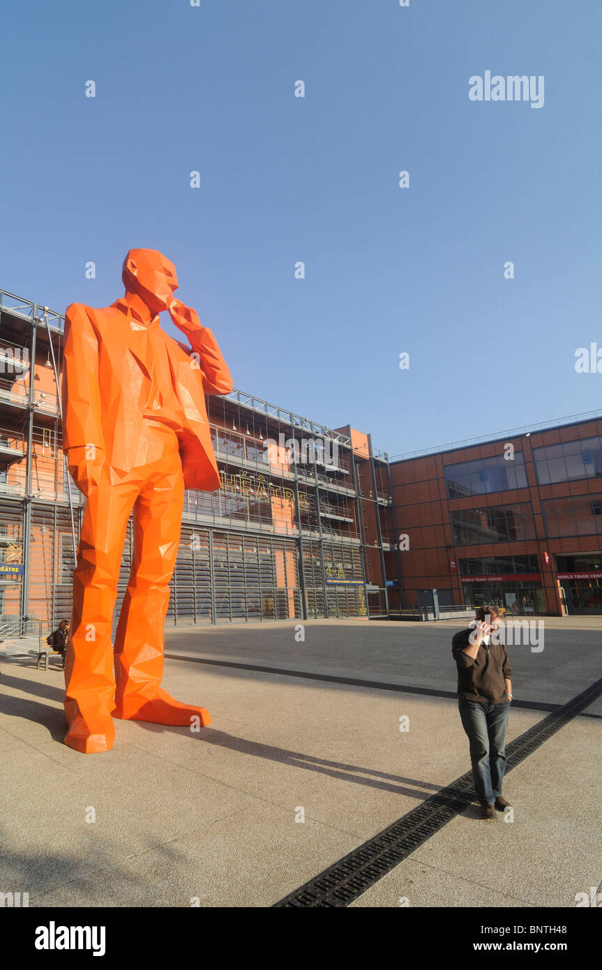 Un uomo con il suo telefono cellulare in prossimità di una gigantesca statua che mostra un uomo con un telefono cellulare la Cité internationale di Lione, in Francia. Foto Stock