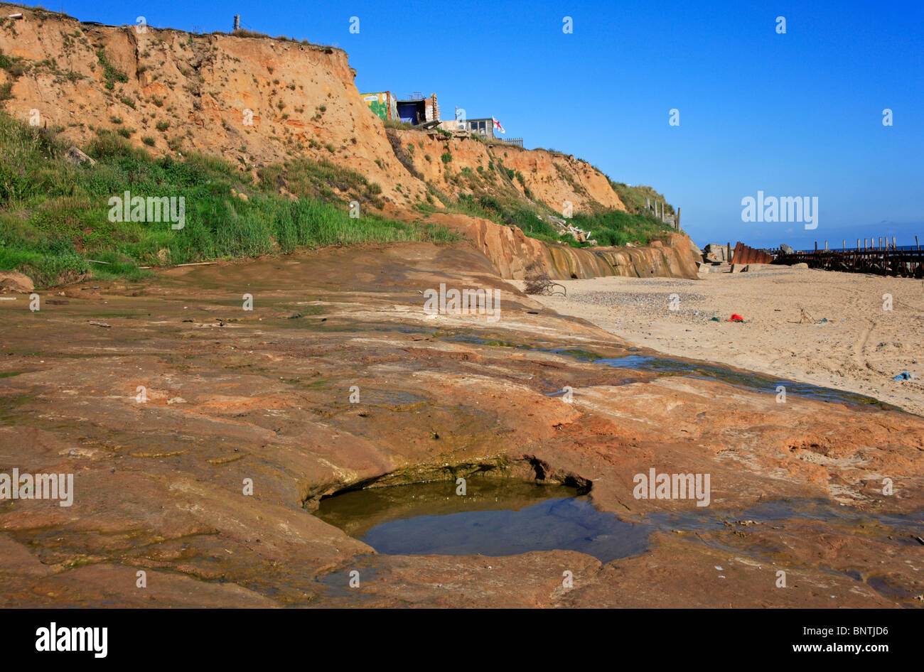 Erosione costiera a Happisburgh, Norfolk, Inghilterra, Regno Unito, con onda della piattaforma di taglio e gli edifici su cliff edge. Foto Stock