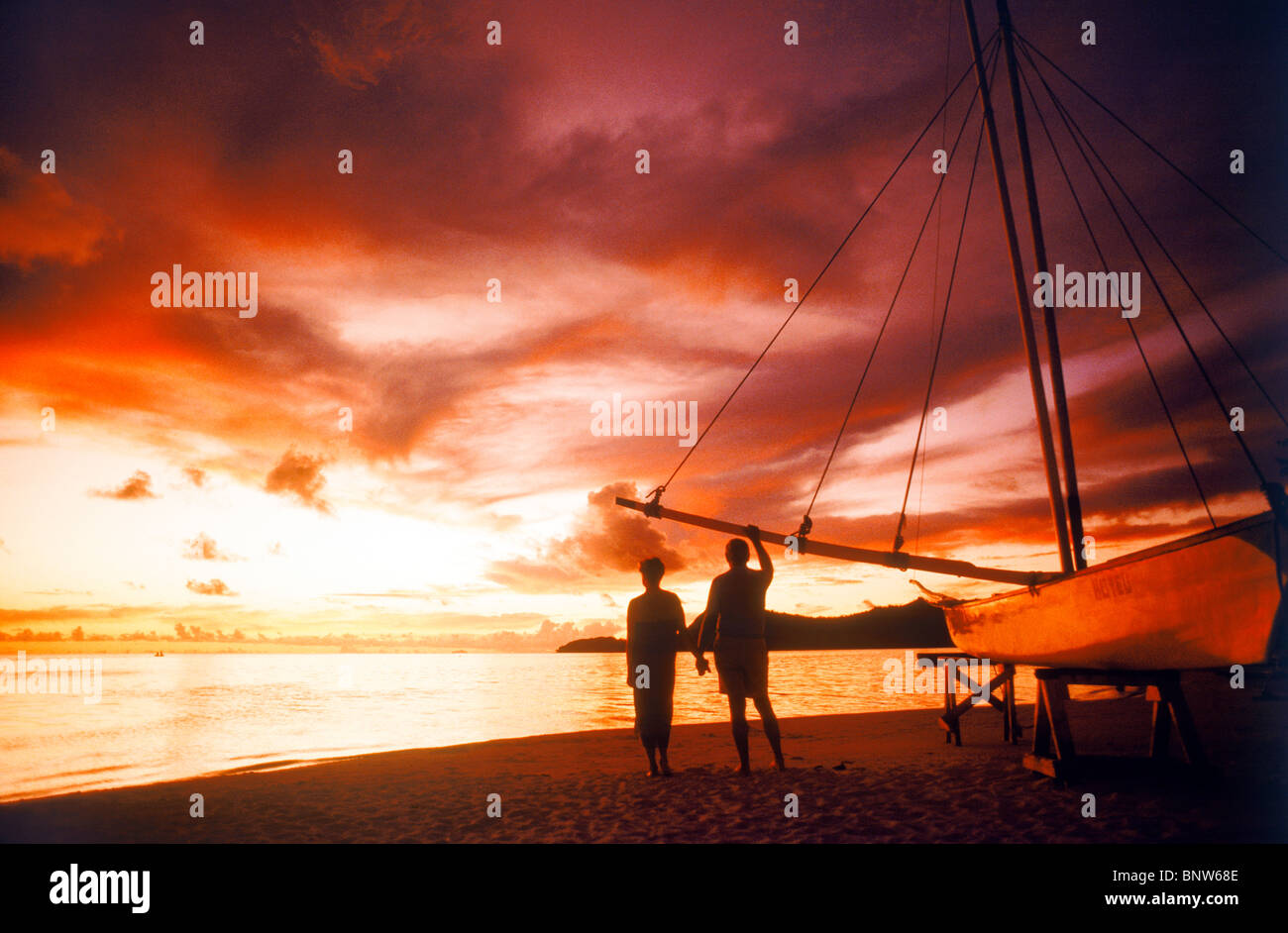 Matura in piedi accanto alla canoa outrigger sulla Bora Bora shore tenendo le mani sotto il tramonto spettacolare sky Foto Stock