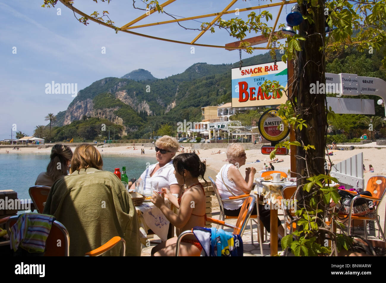 Turisti che si godono il pranzo in spiaggia snack bar a Paleokastritsa sull'isola greca di Corfu Grecia GR Foto Stock