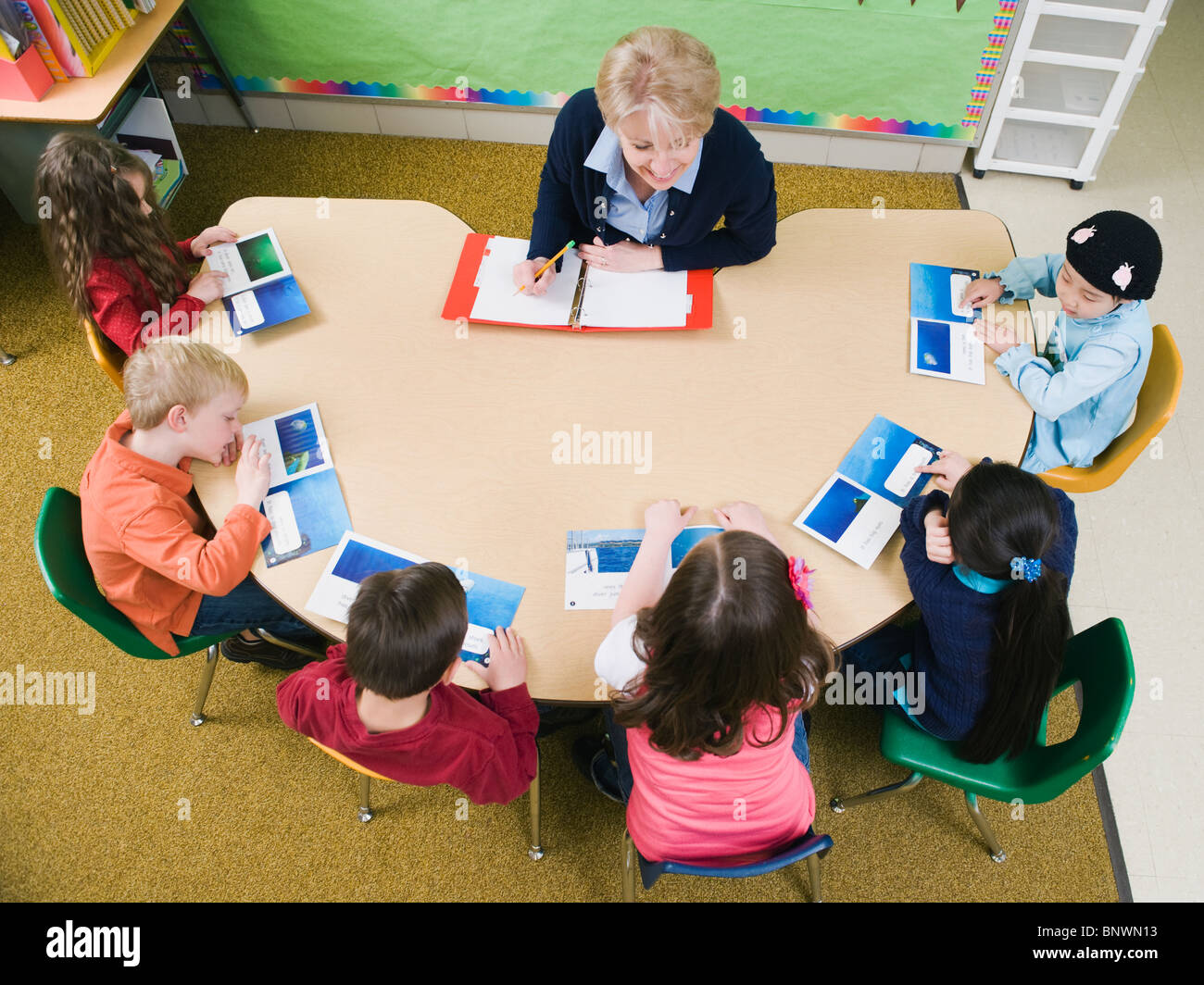 Kindergarten studenti seduti a tavola con il loro insegnante Foto Stock