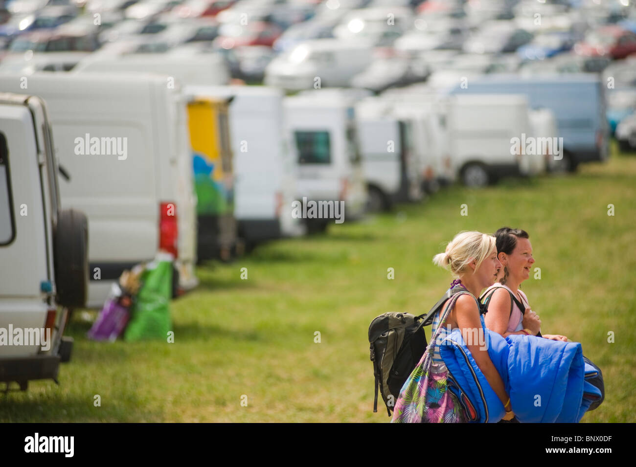 Le persone che lasciano il festival di Glastonbury alla fine del festival con le macchine parcheggiate e furgoni in background. Foto Stock