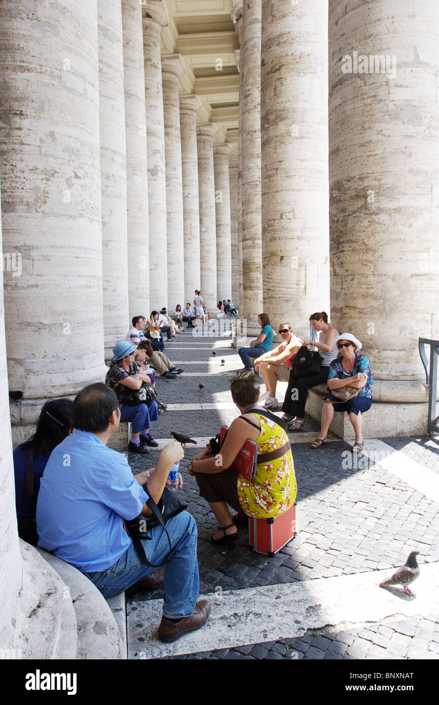 Città del Vaticano Roma. Turisti cattolici in piazza San Pietro seduta per rilassarsi vero il colonnato. Foto Stock