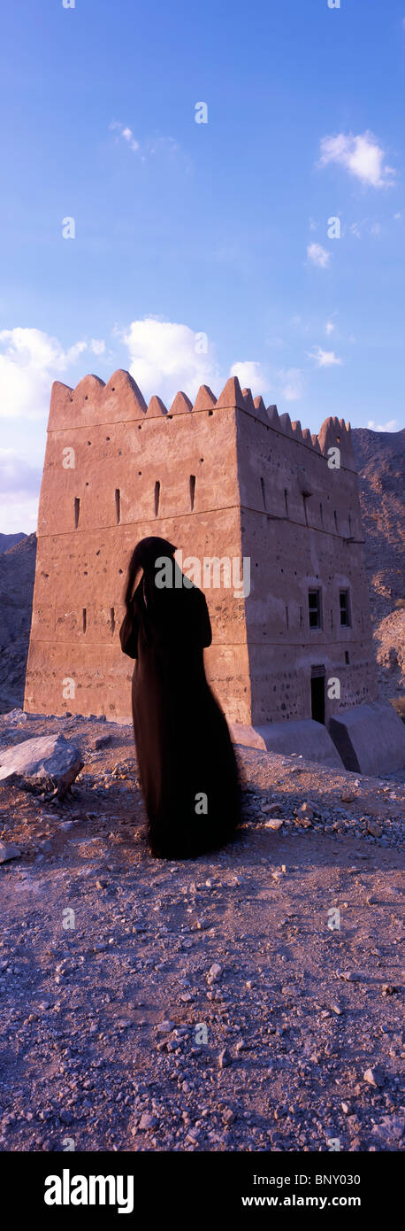 Donna in abaya tradizionale ammirando i resti di una delle torri di avvistamento di Wadi Hayl Summer Palace, Fujairah, U.A.E. Foto Stock