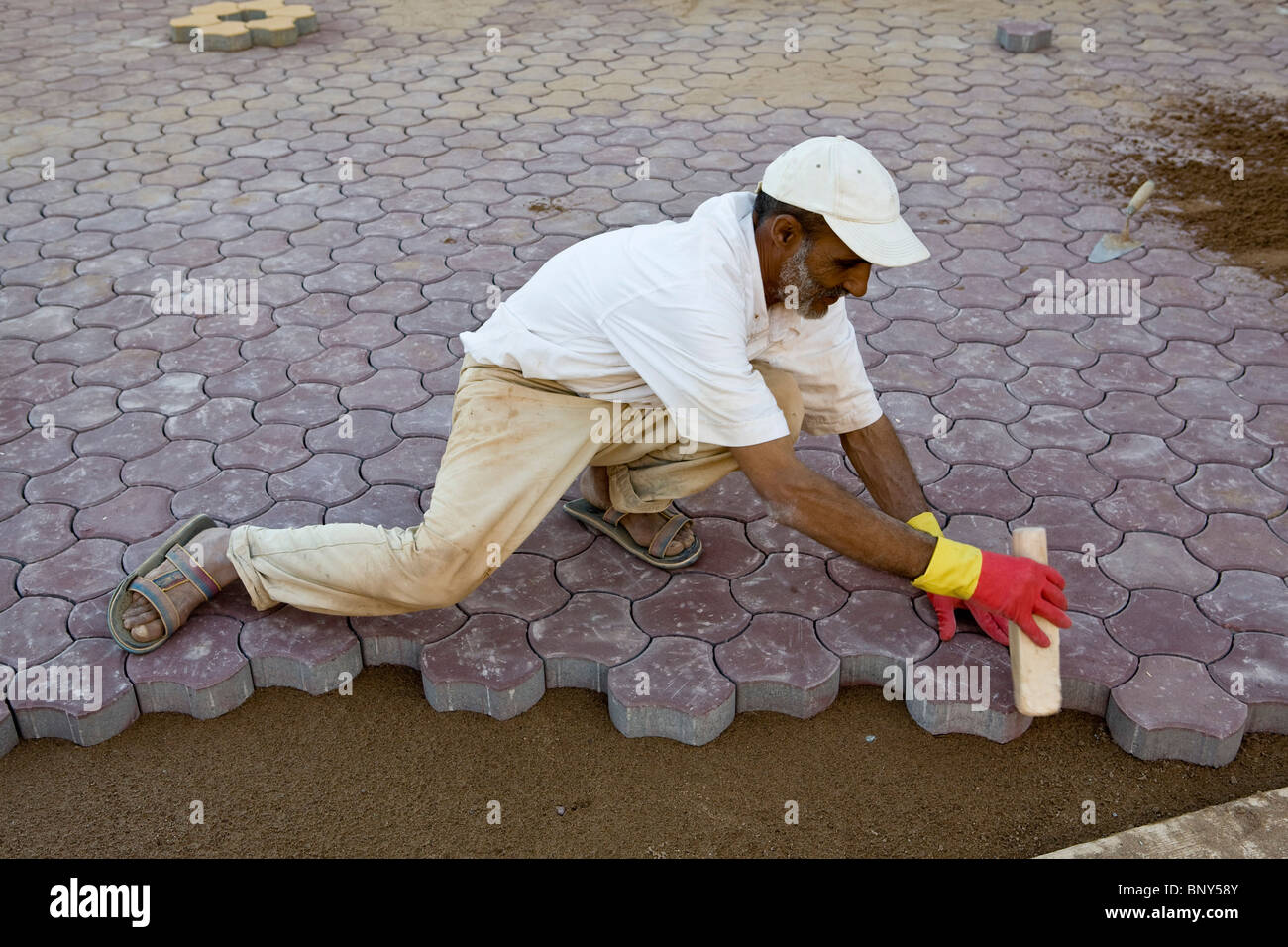 L'uomo installazione ad incastro di pietre per pavimentazione sul terreno in modo da creare il marciapiede, Ouled Berhil, Marocco Foto Stock