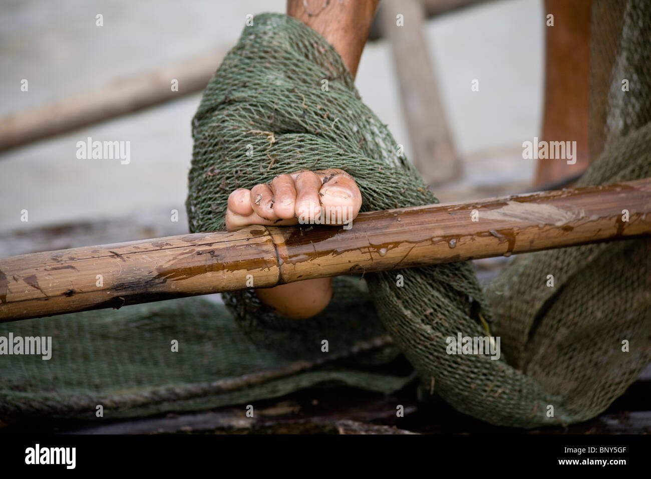 Fisherman's piede sul bordo della sua barca, avvolto in rete da pesca, nella cittadina di Chau Doc, Vietnam Foto Stock