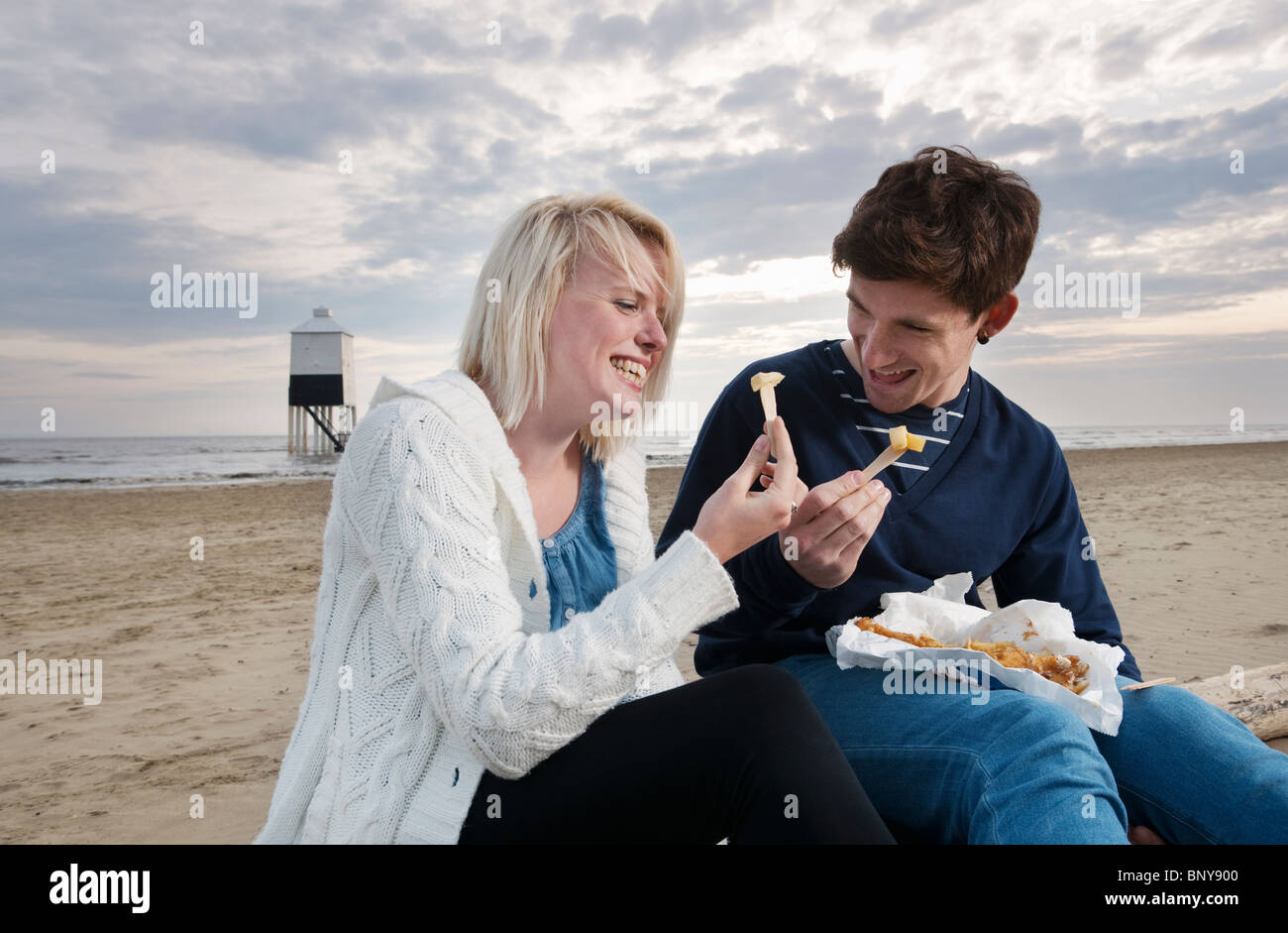 Coppia sulla spiaggia a mangiare pesce e patatine Foto Stock