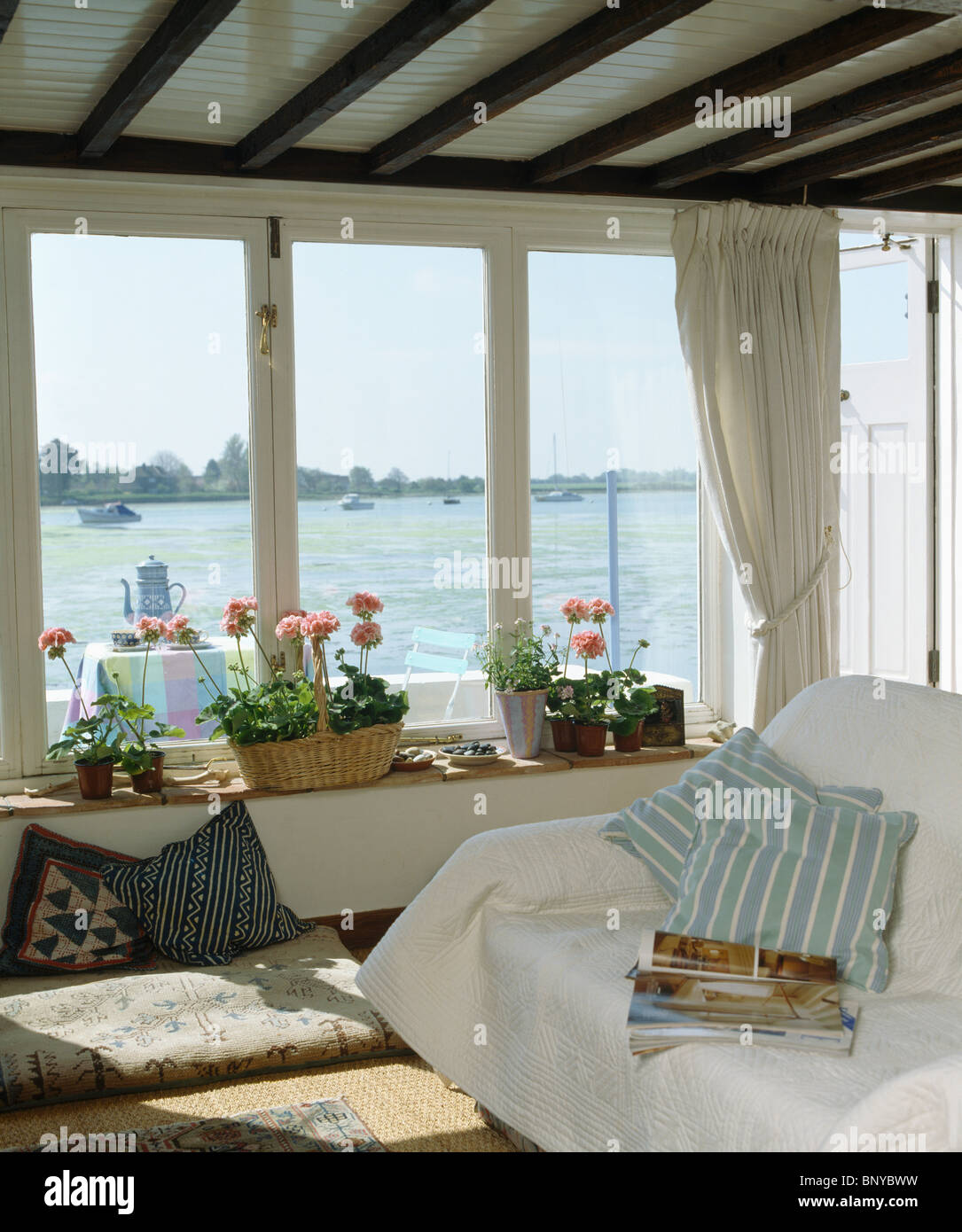 Buttare in bianco e blu cuscino a strisce sul divano in coastal cottage soggiorno con vista del mare attraverso la finestra Foto Stock