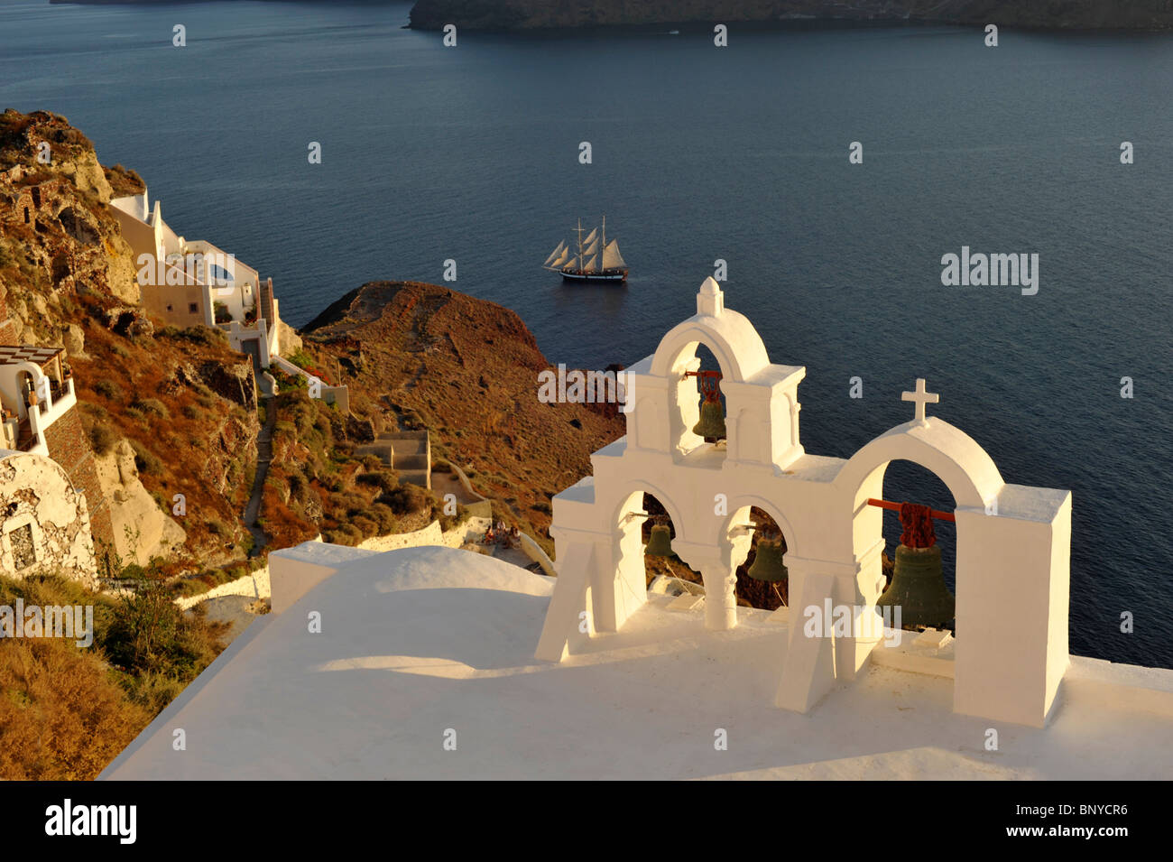 Campanile della chiesa con una nave a vela nella caldera a Oia sull'isola greca di Santorini nelle Cicladi Foto Stock