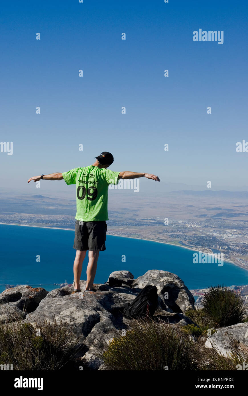 Un uomo intensamente gode del 'al di sopra del mondo' impressione alla Table Mountain summit, Cape Town, Sud Africa. Foto Stock