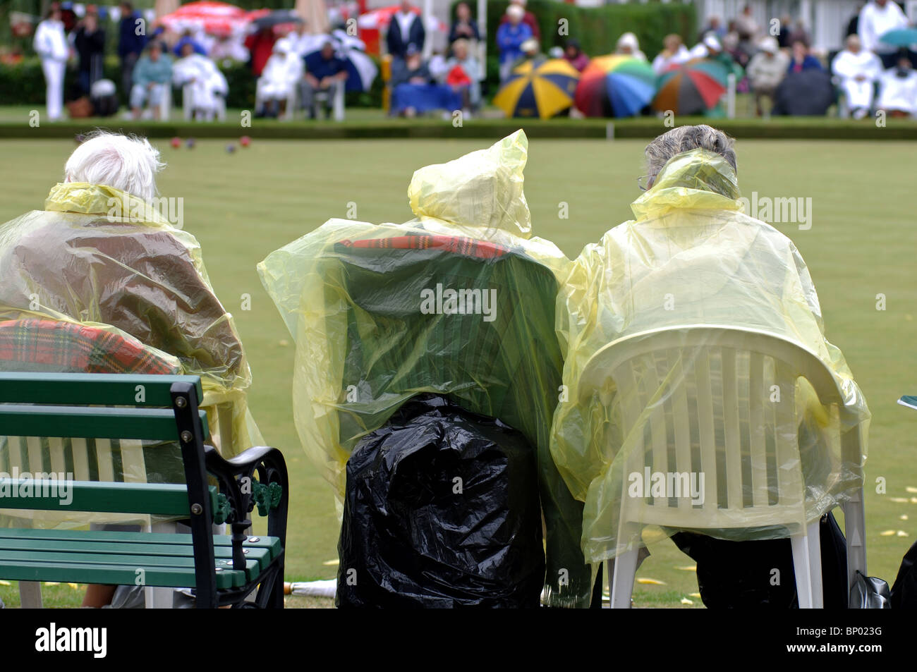 Persone che indossano macks plastica signore guardare partite di bocce Foto Stock