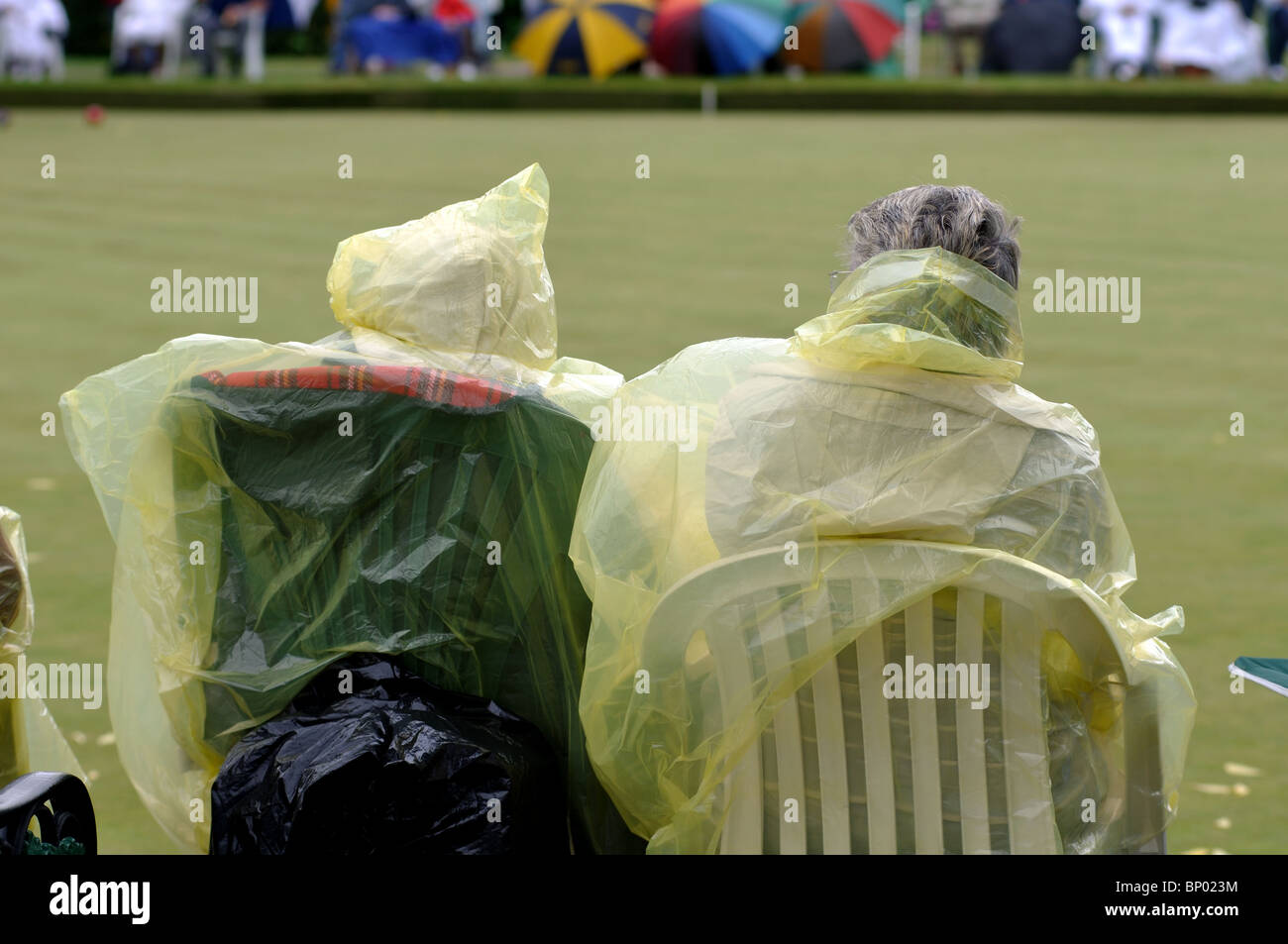 Persone che indossano macks plastica signore guardare partite di bocce Foto Stock
