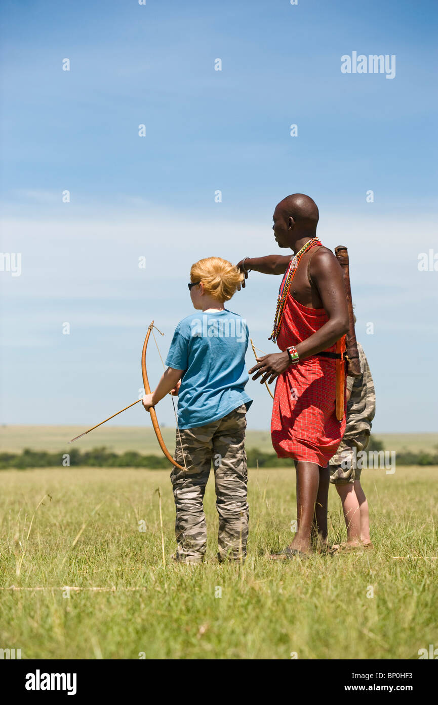 Kenia Masai Mara. Guida Safari, Salaash Morompi Ole, insegna ai bambini di tiro con l'arco stile Masai. (MR) Foto Stock