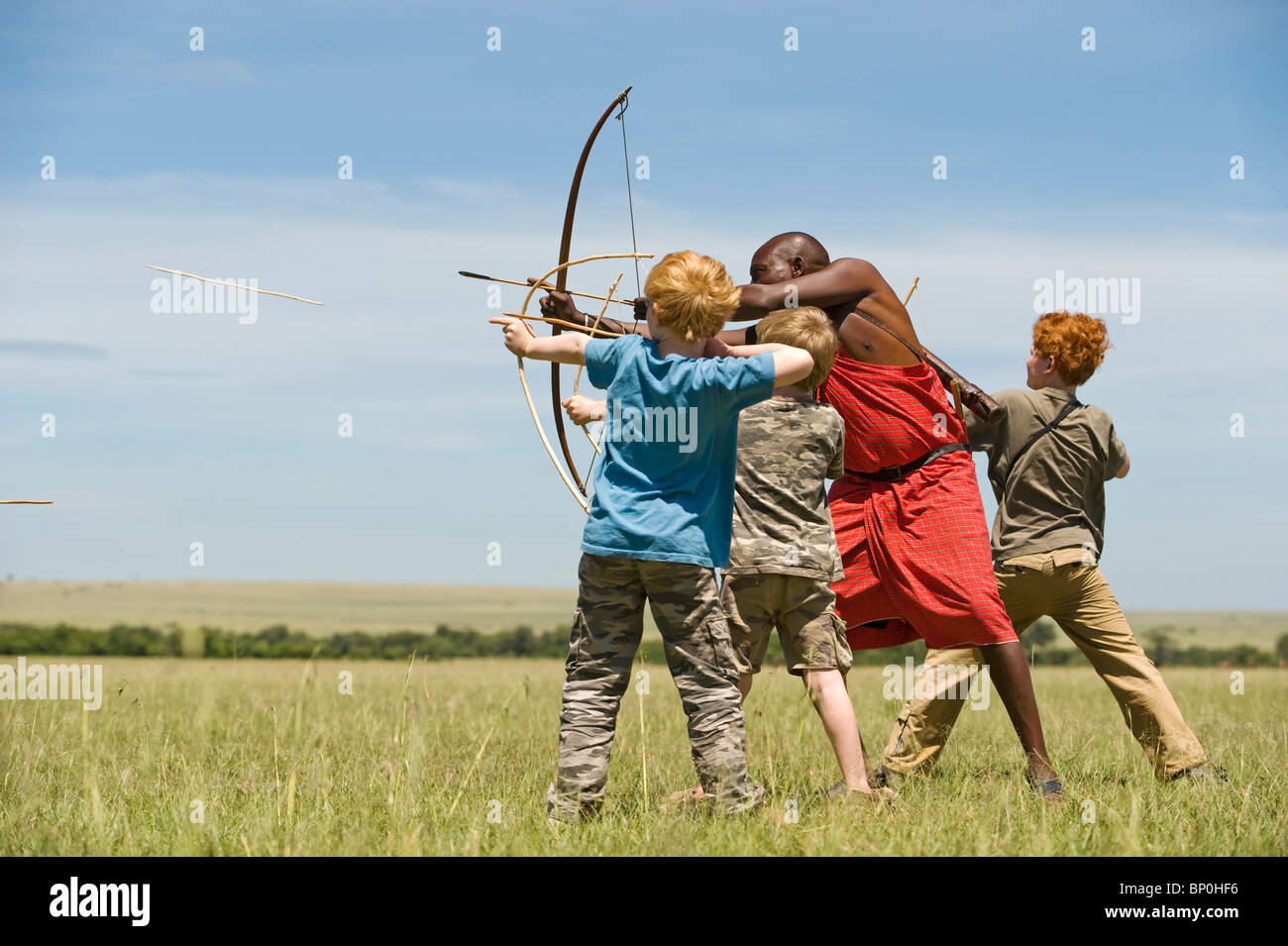 Kenia Masai Mara. Guida Safari, Salaash Morompi Ole, insegna ai bambini di tiro con l'arco stile Masai. (MR) Foto Stock