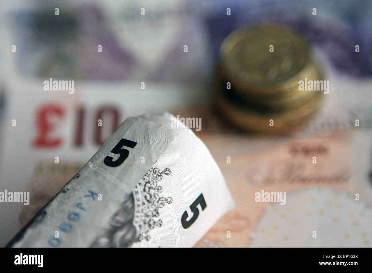 Ripiegate sterling £5 note accanto a una pila di fuori fuoco £2 e £1 monete - Tutto su € 20 e € 10 note Foto Stock