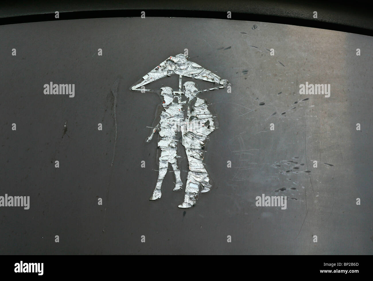 Graffiti sul grigio di una parete metallica a Londra, Regno Unito, di un uomo e di una donna a piedi sotto un ombrello Foto Stock