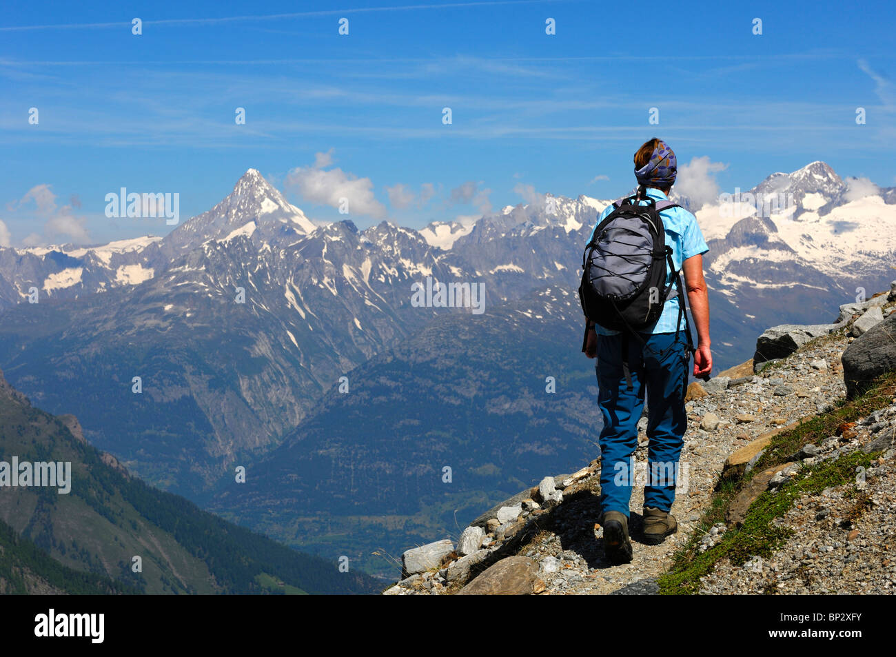 Escursionista femmina escursionismo su uno stretto sentiero di montagna alta sopra la Valle del Rodano in Alpi Pennine, Vallese, Svizzera Foto Stock