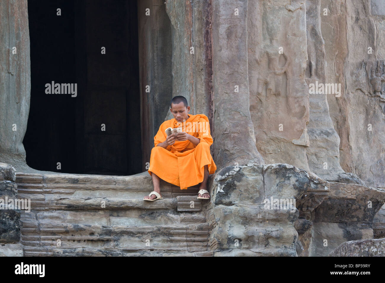 Monaco la lettura mentre è seduto sui gradini a Angkor Wat, Laos Foto Stock