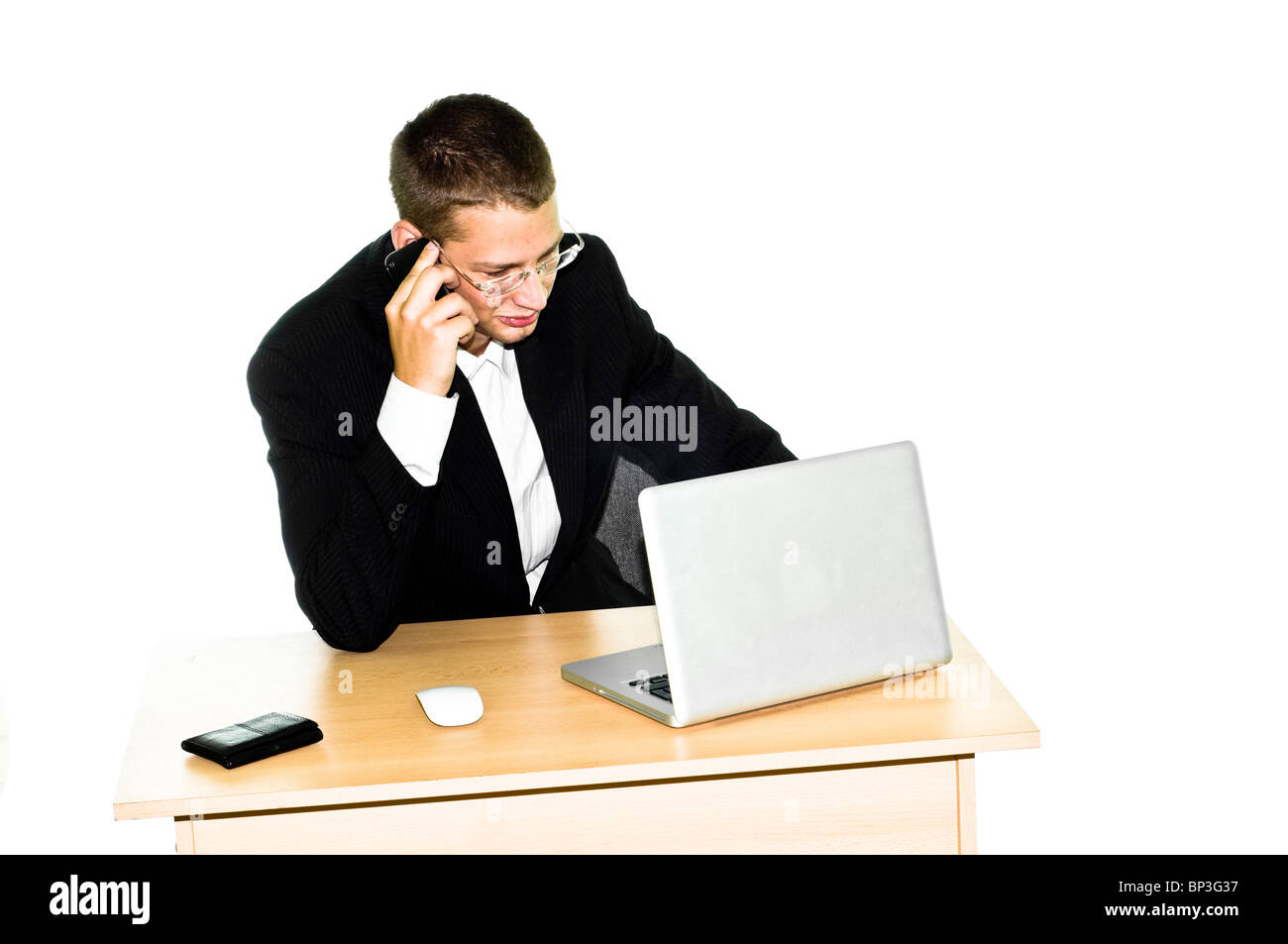 Giovane imprenditore lavorando sulla scrivania con computer portatile, mouse e portafoglio, parlando al telefono cellulare Foto Stock