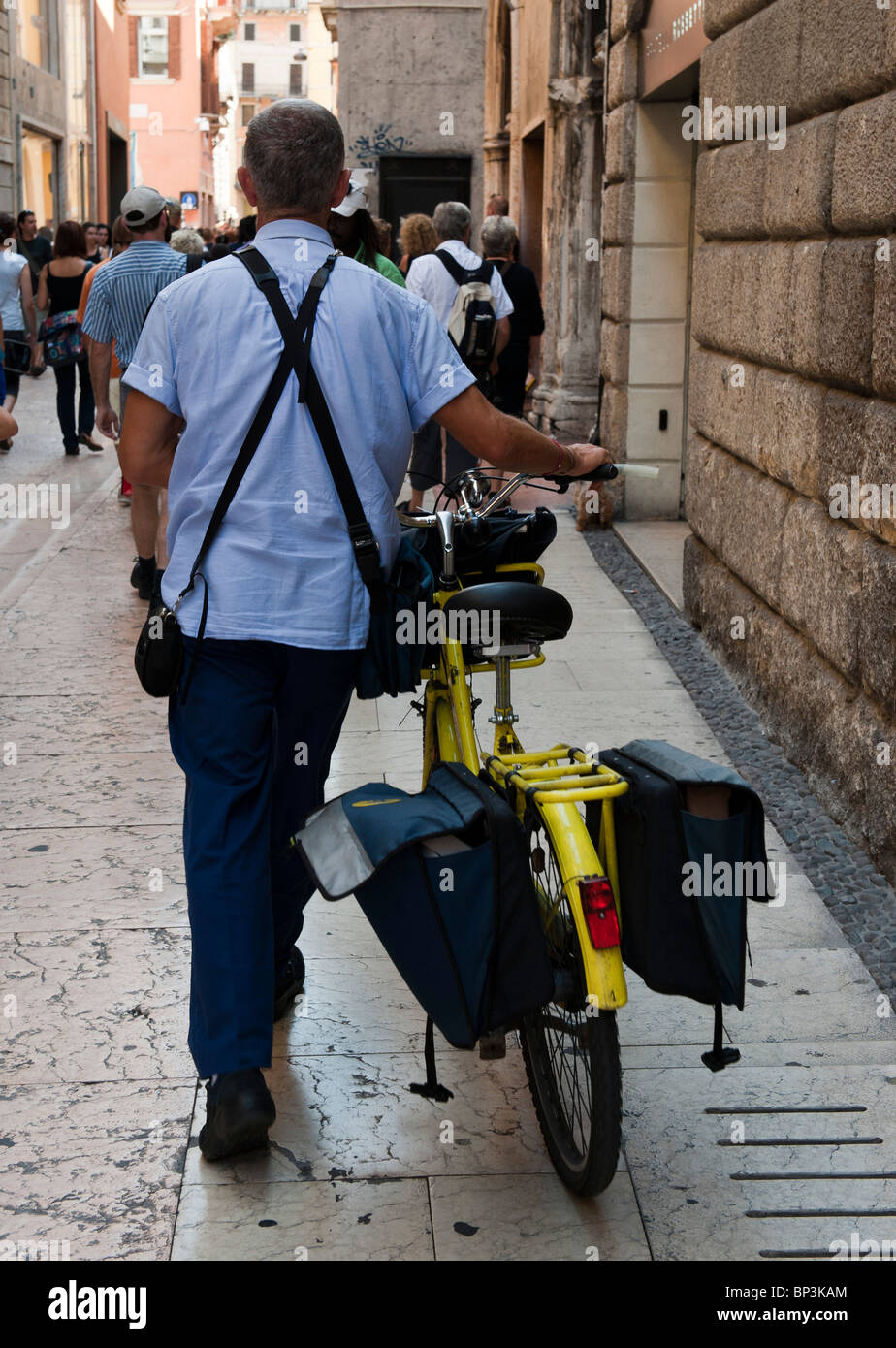 Un postino spingendo la sua bicicletta in una strada a Verona Italia Foto Stock