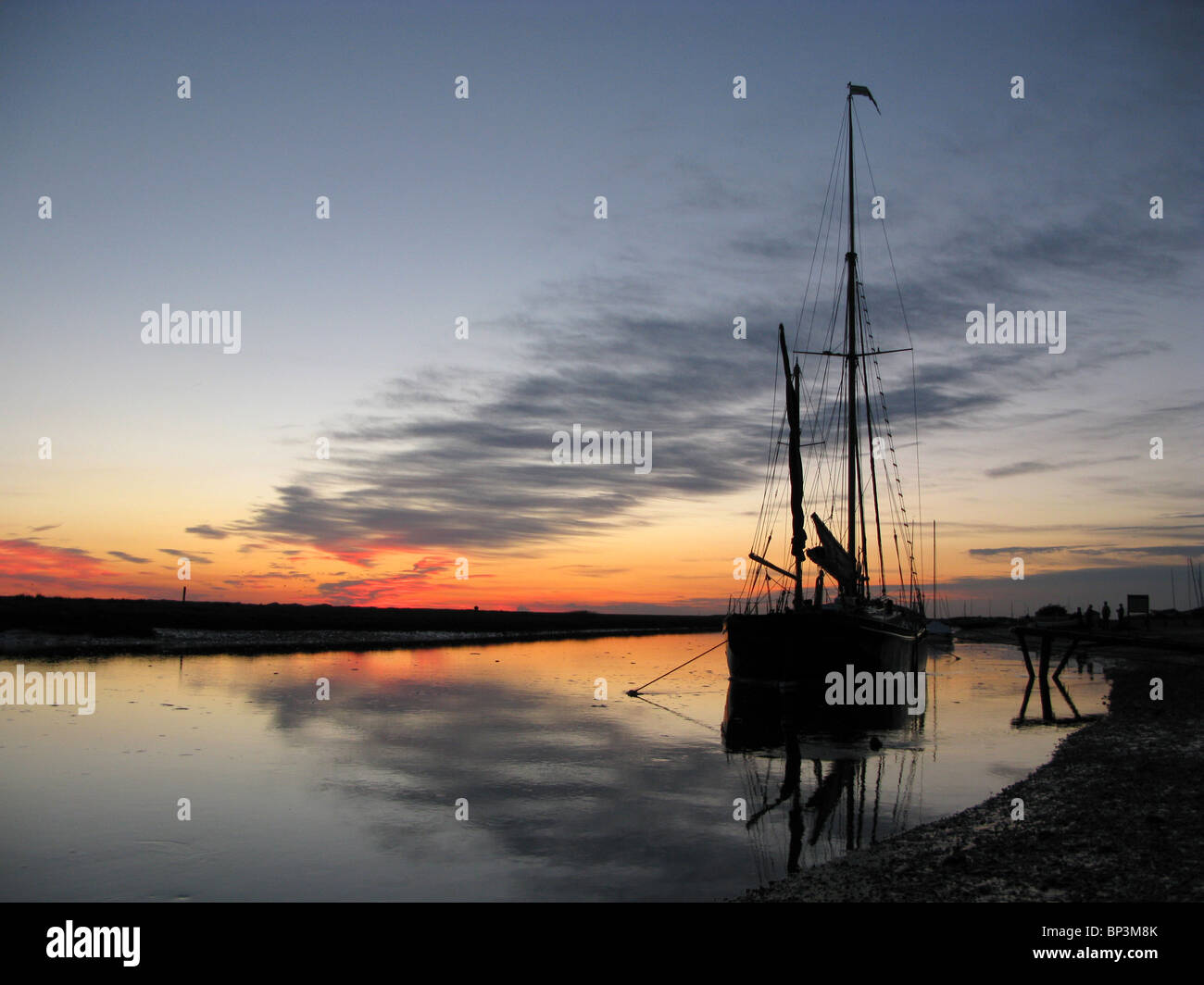 Una barca a vela stagliano contro il tramonto a Blakeney Quay, Norfolk Foto Stock