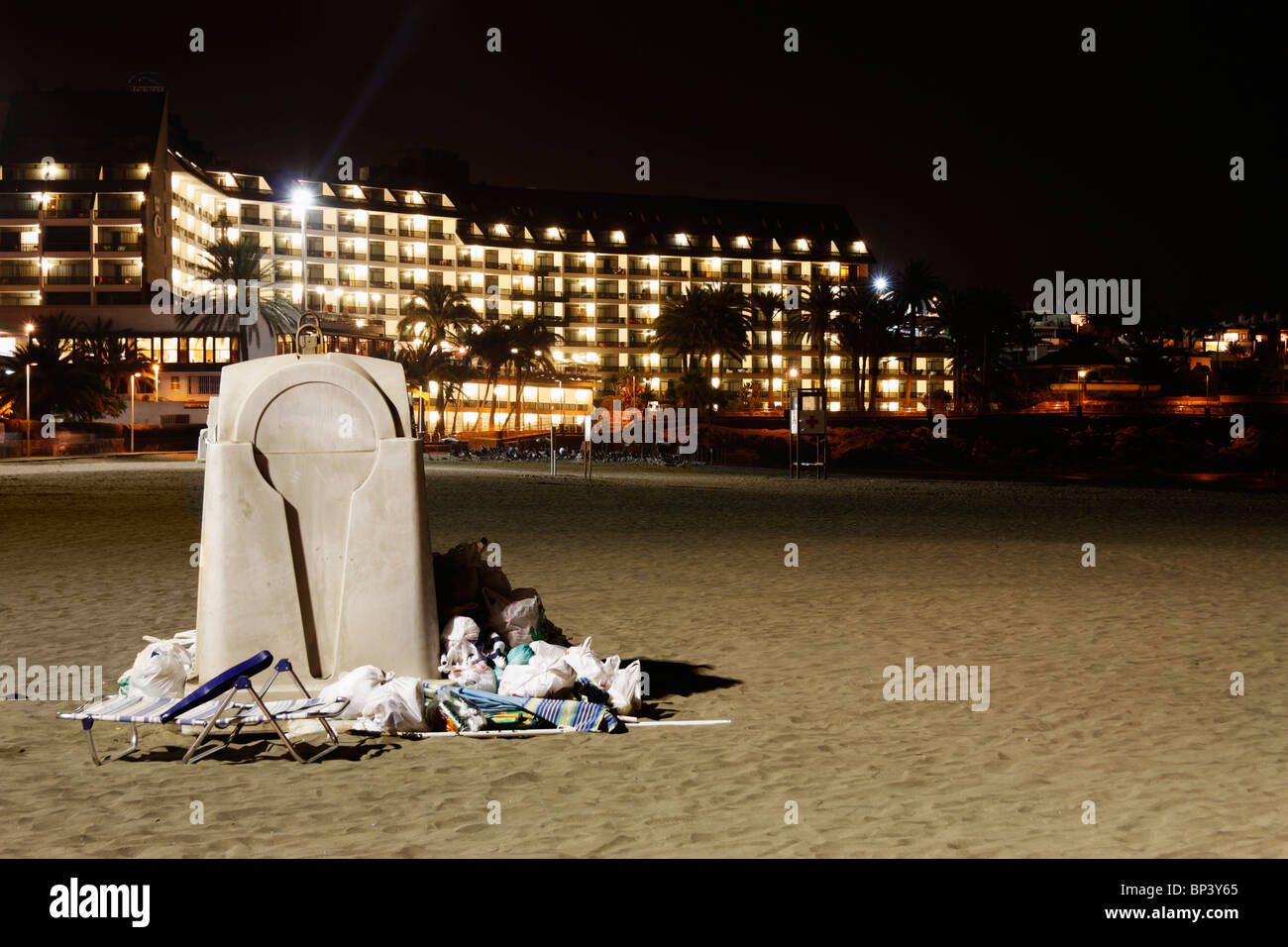 Traboccante contenitore di rifiuti sulla spiaggia in Spagna con grandi hotel in background Foto Stock