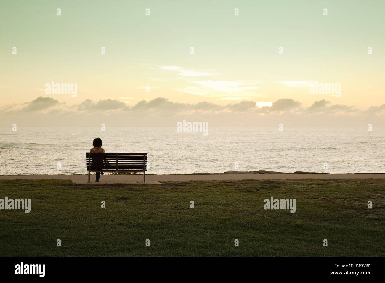 Donna seduta su un banco di lavoro in posizione di parcheggio la visione di sunrise tramonto sull'oceano Foto Stock