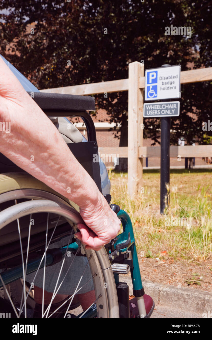 Scena quotidiana di anziani donna seduta su una sedia a rotelle in auto parcheggiate in blue badge parcheggio disabili bay e segno per gli utenti di sedia a rotelle solo Inghilterra REGNO UNITO Foto Stock