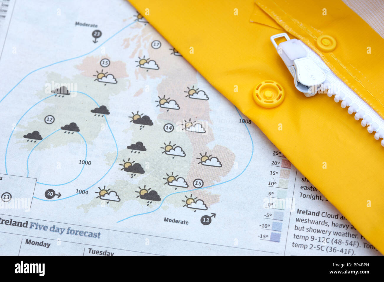 Giaccone impermeabile giallo e zip giacendo attraverso le previsioni meteo in un giornale Foto Stock