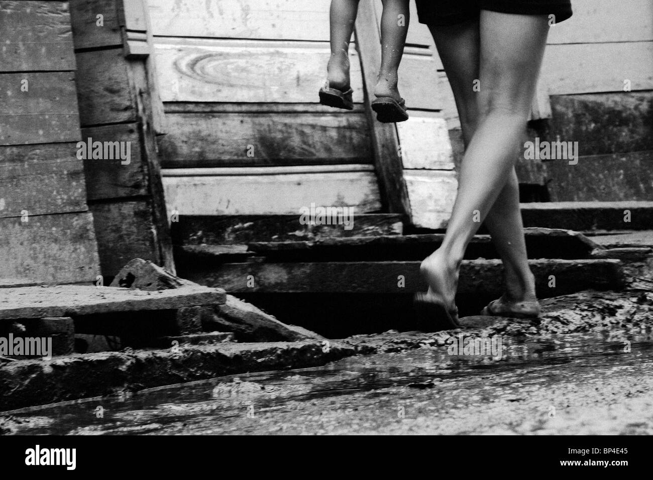 Una giovane madre che porta il suo bambino su fondi fangosi, strada non pavimentata in una piccola comunità di fiume São Paulo de Olivença, Brasile. Foto Stock