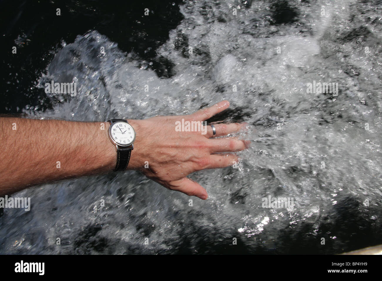 Una mano d'uomo posato sul lato di una barca lasciando scorrere l'acqua attraverso le sue dita modello rilasciato Foto Stock