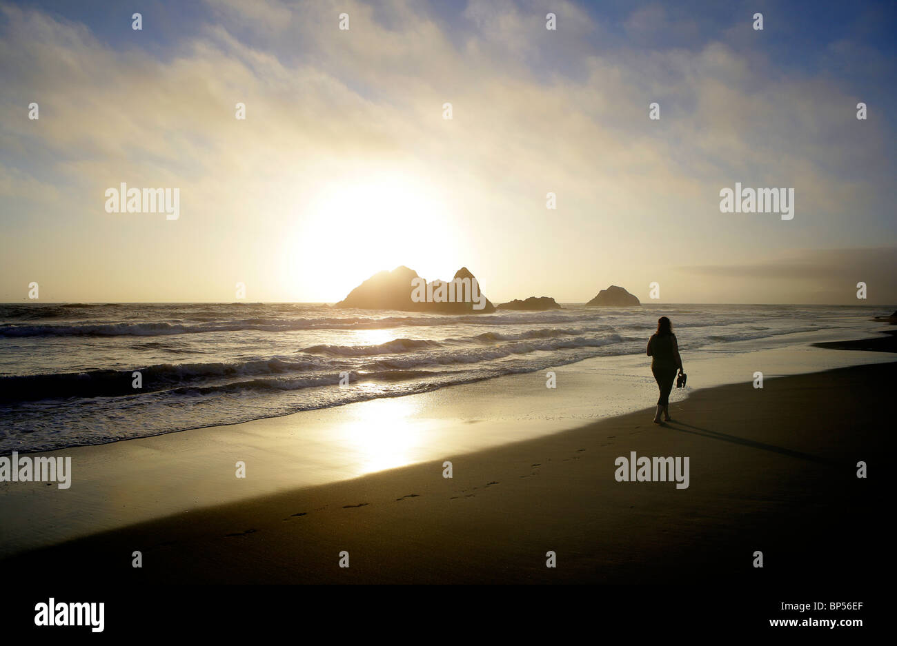 Una donna che cammina su una spiaggia deserta al tramonto Foto Stock