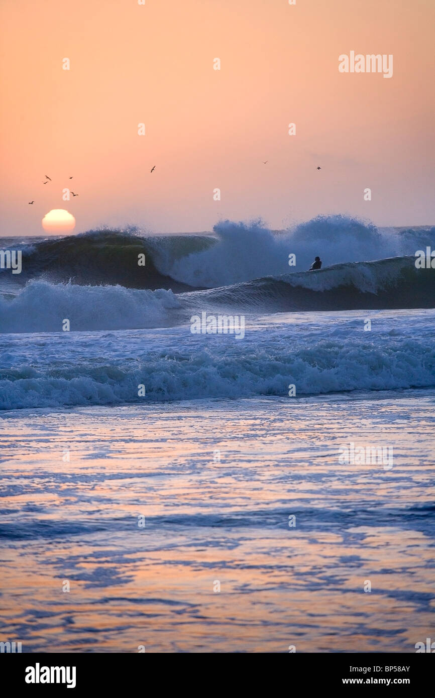 Un surfista in onde al tramonto Foto Stock