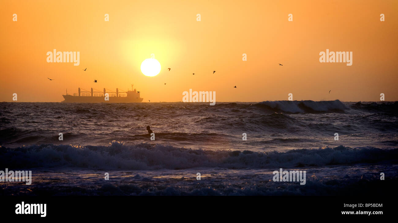 La silhouette di una nave cargo al tramonto con un surfista in primo piano di tiro fuori Ocean Beach in San Francisco Foto Stock