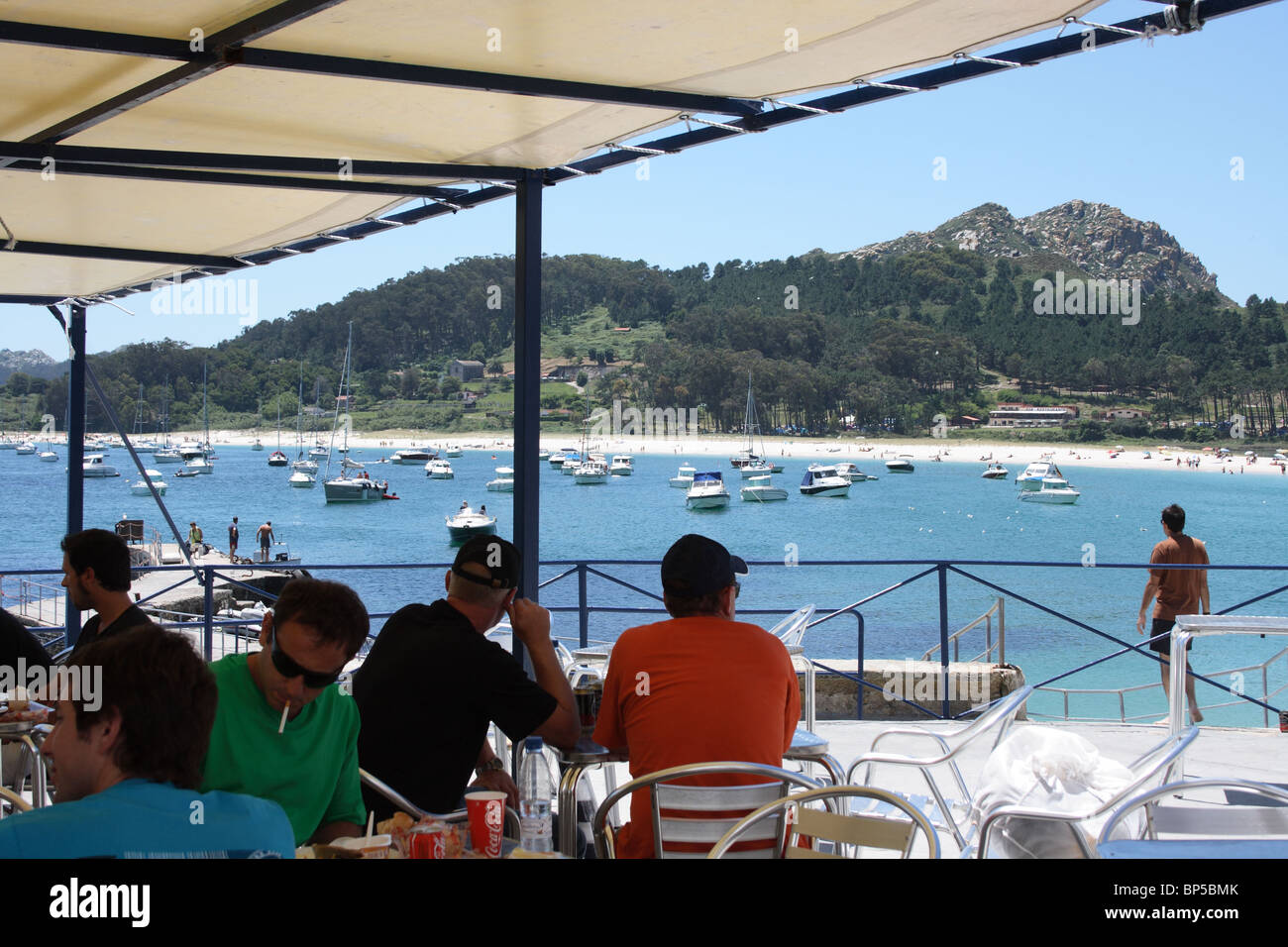 Le persone al cafe esterno tavoli del ristorante sulla spiaggia, Isla de Monte Faro, Isole Cies, Vigo, Galizia, Spagna, spiaggia e barche Foto Stock