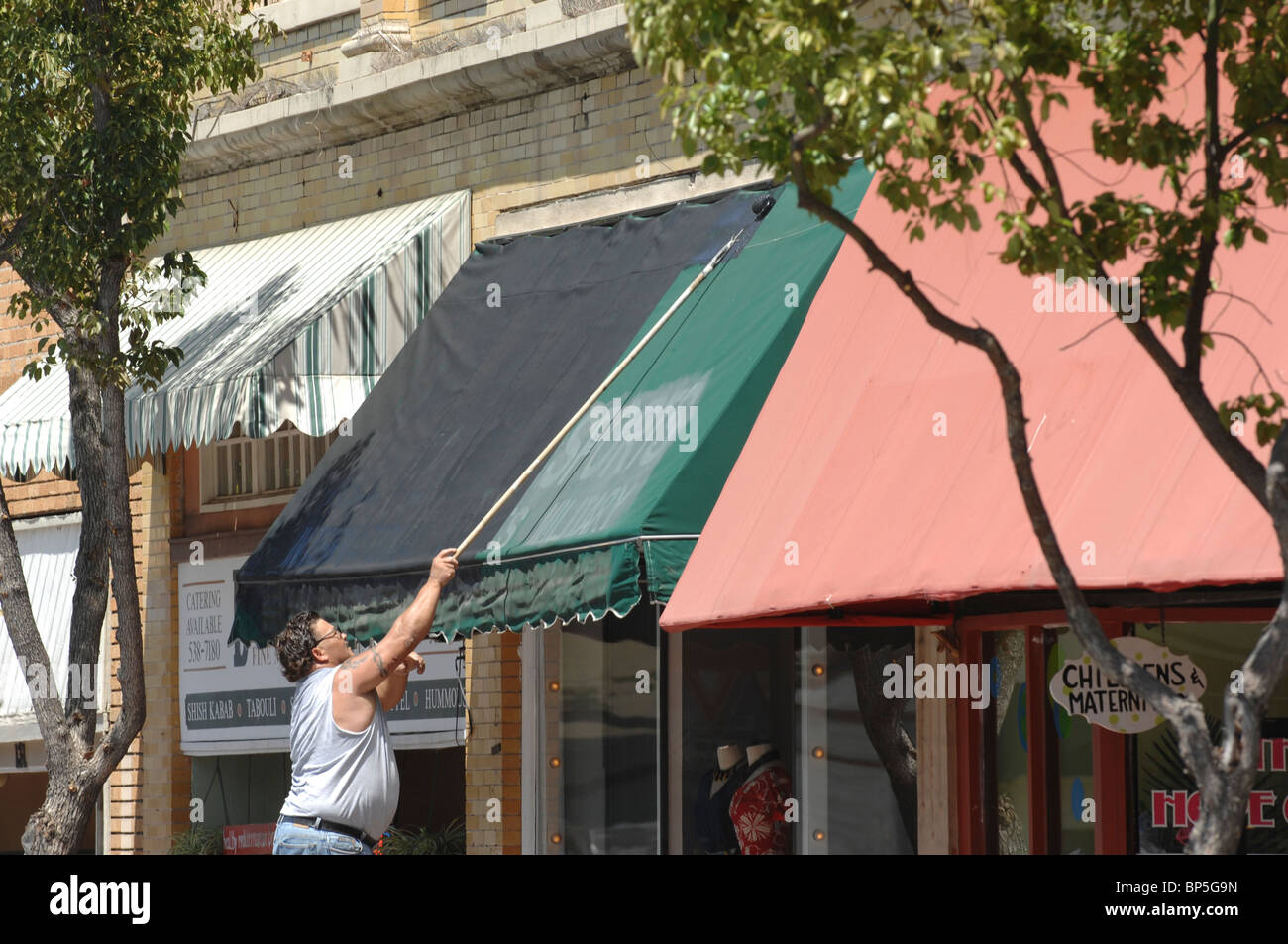 Un uomo su una scala di verniciatura di un telo verde sopra la finestra storefront. Foto Stock