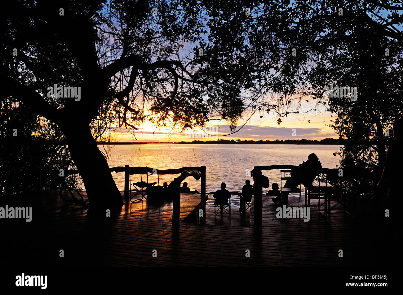 La gente seduta su un mazzo di Guma Lagoon Lodge, Okavango Delta, Repubblica di Botswana, Sud Africa Foto Stock