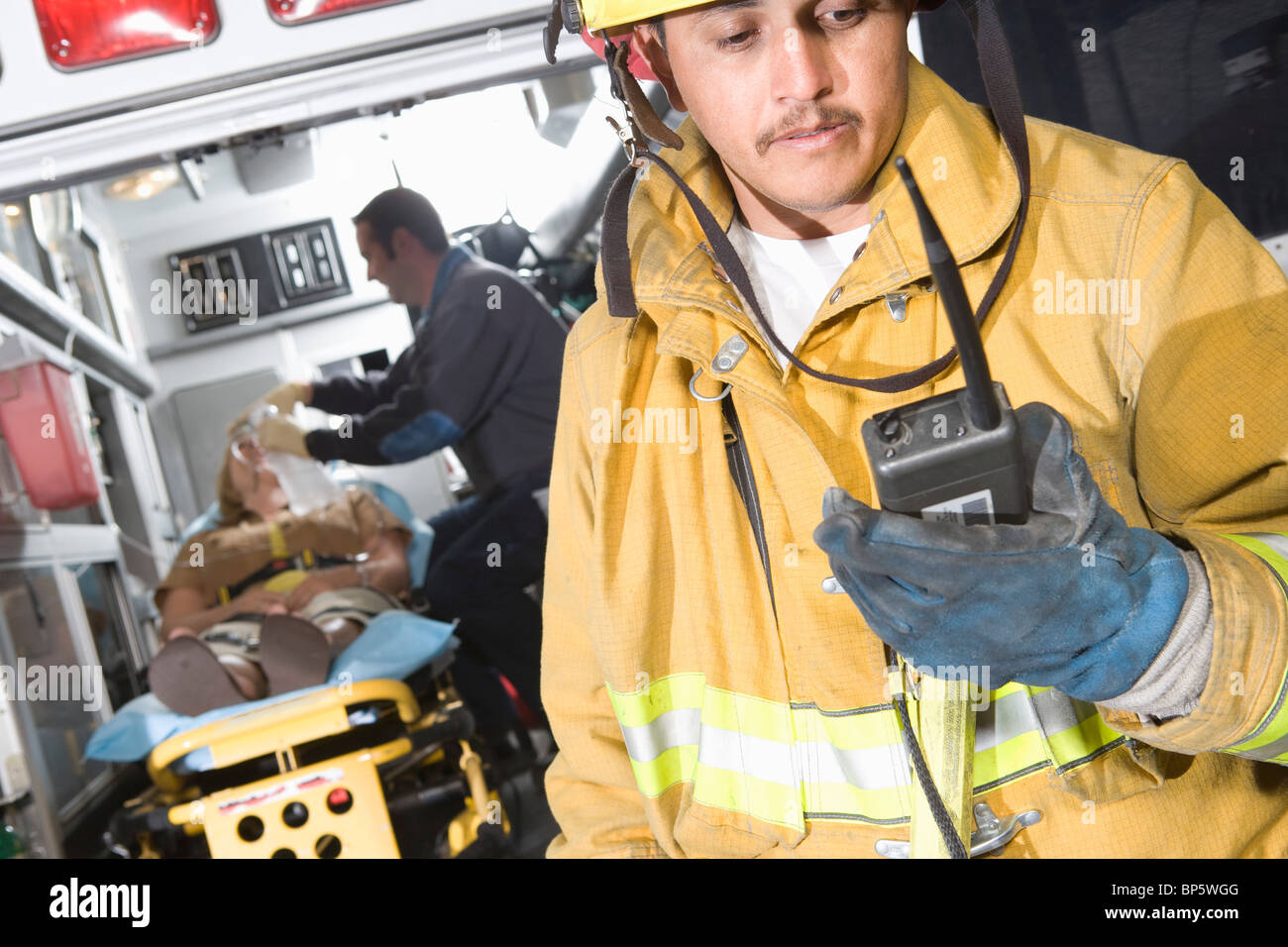 Vigile del fuoco utilizzando la radio, paramedic tendente vittima Foto Stock