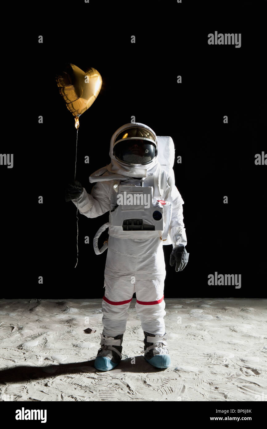 Un astronauta sulla luna tenendo un cuore a forma di palloncino elio Foto Stock